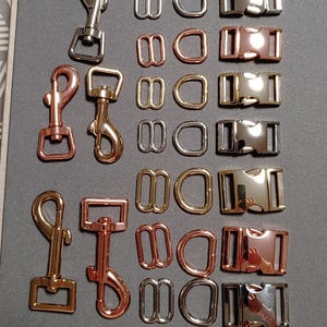 May include: An assortment of metal hardware components in various finishes, including silver, copper, and gold. The collection features swivel clasps, D-rings, tri-glides, and side-release buckles, suitable for crafting and accessories.