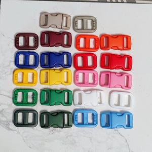 May include: A collection of colorful plastic buckles in various shades, including brown, red, orange, blue, yellow, pink, green, white, and light blue. These buckles are designed with a two-piece, side-release mechanism.