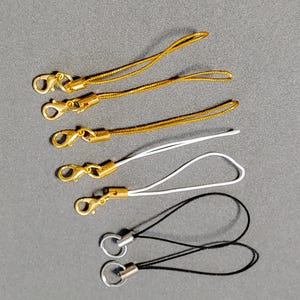 May include: Five gold keychains with a gold clasp and a gold cord. One white keychain with a gold clasp and a white cord. Two black keychains with a silver clasp and a black cord.