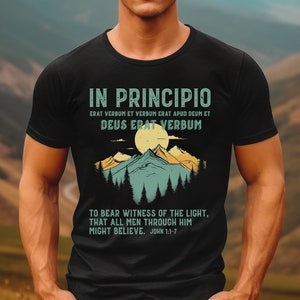May include: Black t-shirt with a mountain and sun graphic. The text reads "IN PRINCIPIO, ERAT VERBUM ET VERBUM ERAT APUD DEUM ET DEUS ERAT VERBUM, TO BEAR WITNESS OF THE LIGHT, THAT ALL MEN THROUGH HIM MIGHT BELIEVE. JOHN 1:1-7."