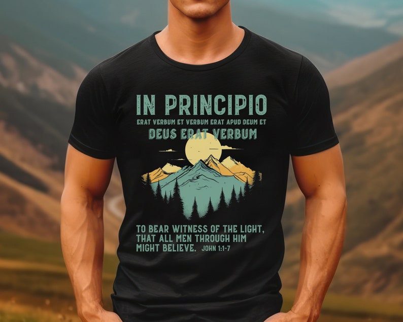 May include: Black t-shirt with a mountain and sun graphic. The text reads "IN PRINCIPIO, ERAT VERBUM ET VERBUM ERAT APUD DEUM ET DEUS ERAT VERBUM, TO BEAR WITNESS OF THE LIGHT, THAT ALL MEN THROUGH HIM MIGHT BELIEVE. JOHN 1:1-7."