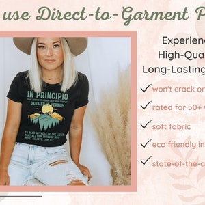 May include: Black t-shirt with a mountain graphic and the text "IN PRINCIPIO DEUS ERAT VERBUM". The image also includes text that says "We use Direct-to-Garment Print" and "Experience High-Quality, Long-Lasting Prints".