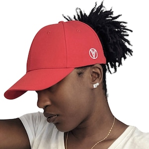 May include: A red baseball cap with a white circle logo on the back. The cap has a ponytail hole and is being worn by a person with dark hair.