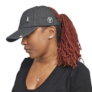 May include: A black denim baseball cap with a ponytail hole and a white circle logo with a letter V inside. The cap has distressed detailing.