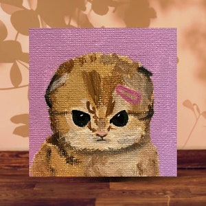 May include: A painting of a brown tabby cat with a pink bandage on its head. The cat has a grumpy expression and is looking directly at the viewer. The painting is on a purple background.