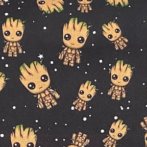 May include: A black fabric with a repeating pattern of small, brown, cartoon characters with green hair and large eyes. The background is black with white dots.