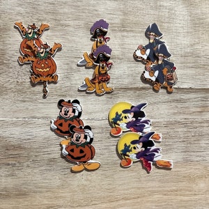 May include: A collection of flat, die-cut acrylic charms featuring Disney characters in Halloween costumes. The set includes Tigger in a pumpkin, Pluto as a pirate, Tigger as a pirate, Mickey Mouse in a pumpkin, and Minnie Mouse as a witch.