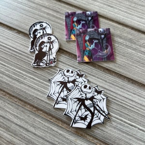 May include: A set of Nightmare Before Christmas themed stickers featuring Jack Skellington and Sally. The stickers are printed on white paper with black ink. There are three different designs: Jack Skellington in a spiderweb, Jack Skellington and Sally in a graveyard, and Jack Skellington and Sally in a moon.