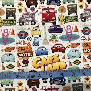 Pu&ograve; includere: Un tessuto colorato con un motivo ripetitivo di auto, camion e altri veicoli del film Cars della Disney Pixar. Il tessuto include il testo "Cars Land" e vari altri testi del film, come "Tow Mater" e "Cozy Cone Motel".