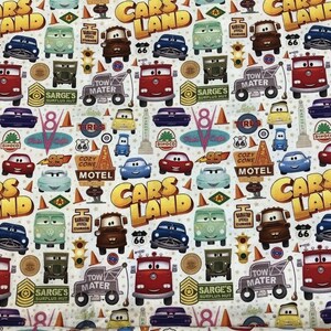 Pu&ograve; includere: Un tessuto bianco con un motivo ripetuto di immagini a tema Cars Land. Le immagini includono auto, camion, cartelli e le parole "Cars Land".
