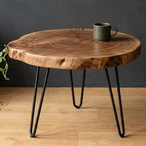 Könnte beinhalten: Ein runder Beistelltisch aus Holz mit natürlicher Kante und dunkelbraunem Finish. Der Tisch wird von drei schwarzen Haarnadelbeinen getragen. Eine grüne Tasse steht darauf. Der Tisch hat einen Durchmesser von ca. 61 cm.