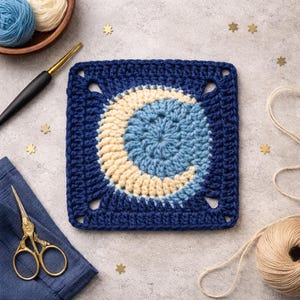 Può includere: Un quadrato all'uncinetto blu navy con un design a mezzaluna in azzurro e crema. I materiali per l'artigianato circondano il quadrato, tra cui filo, un uncinetto, forbici e coriandoli dorati a forma di stella.