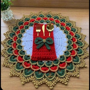 Può includere: Un sottopiatti natalizio fatto a mano, all'uncinetto, con un portatovaglioli rosso e posate dorate. Il sottopiatti presenta un centro bianco, circondato da bordi smerlati rossi, verdi e dorati. Un fiocco verde adorna il portatovaglioli rosso.