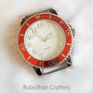 May include: A silver watch with a white face and red bezel. The watch face has black numbers and hands. The watch is quartz.