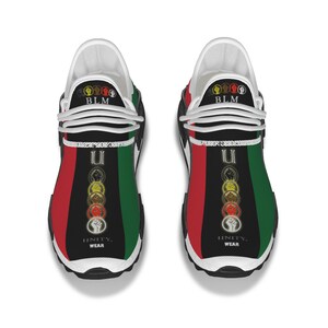 May include: A pair of white sneakers with black, red, and green accents. The shoes feature a graphic design with the words "Unity Wear" and "BLM" along with a series of raised fists.