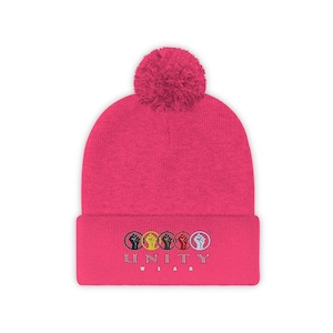 May include: Pink knitted beanie with a pom pom on top and a white embroidered logo that says "UNITY WEAR" with five raised fists in a circle.