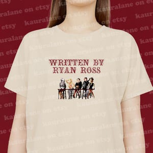 Puede incluir: Una camiseta beige con un estampado gráfico rojo de un grupo de personas sentadas en una mesa. El texto "Written by Ryan Ross" está impreso en rojo sobre el gráfico.