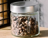 60g Perkele fair. Arabica GM coffee beans completely in the glass container and lid matching the Perkele UNO manual coffee grinder with ceramic grinder