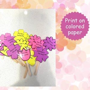 May include: A collection of flower-shaped cutouts in pink, yellow, and purple, each with a wooden stick handle. The cutouts feature phrases like "Jump," "Reach for the sky," and "Fly like a butterfly." A pink circular sign says "Print on colored paper."