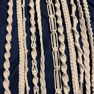 May include: A collection of 12 macrame cord strands in various knot patterns, all in a natural off-white color. The cords are arranged vertically against a dark blue background.
