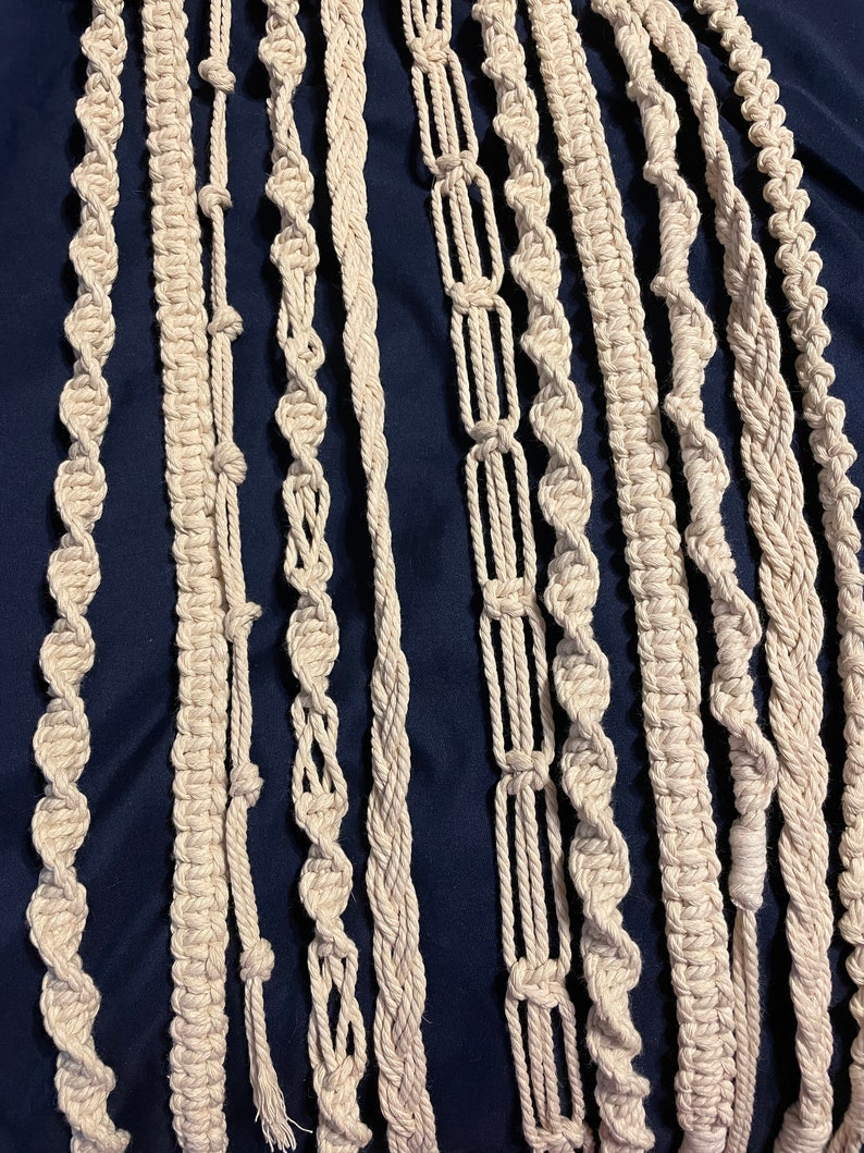 May include: A collection of 12 macrame cord strands in various knot patterns, all in a natural off-white color. The cords are arranged vertically against a dark blue background.