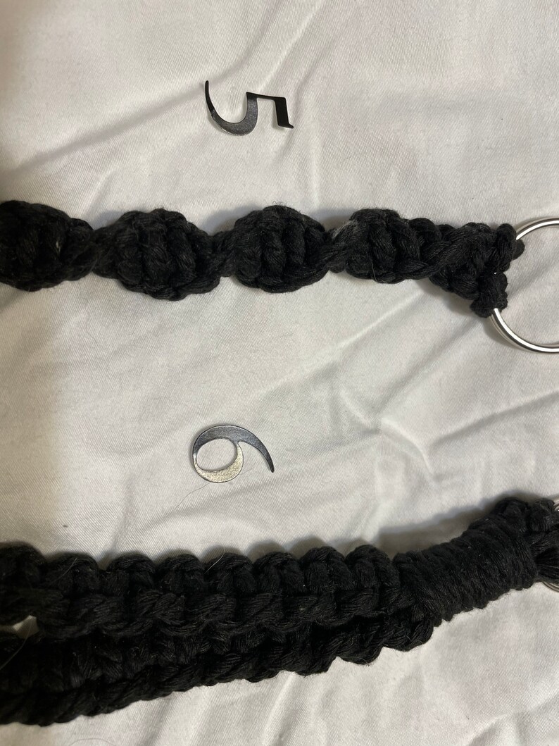 May include: Two black rope keychains with silver metal rings. The keychain on top has the number "5" on a white background. The keychain on the bottom has the number "6" on a white background.