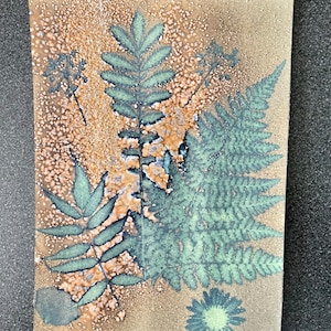 May include: A brown paper background with a green fern leaf, a green flower, and a few other green leaves. The background has a speckled texture.
