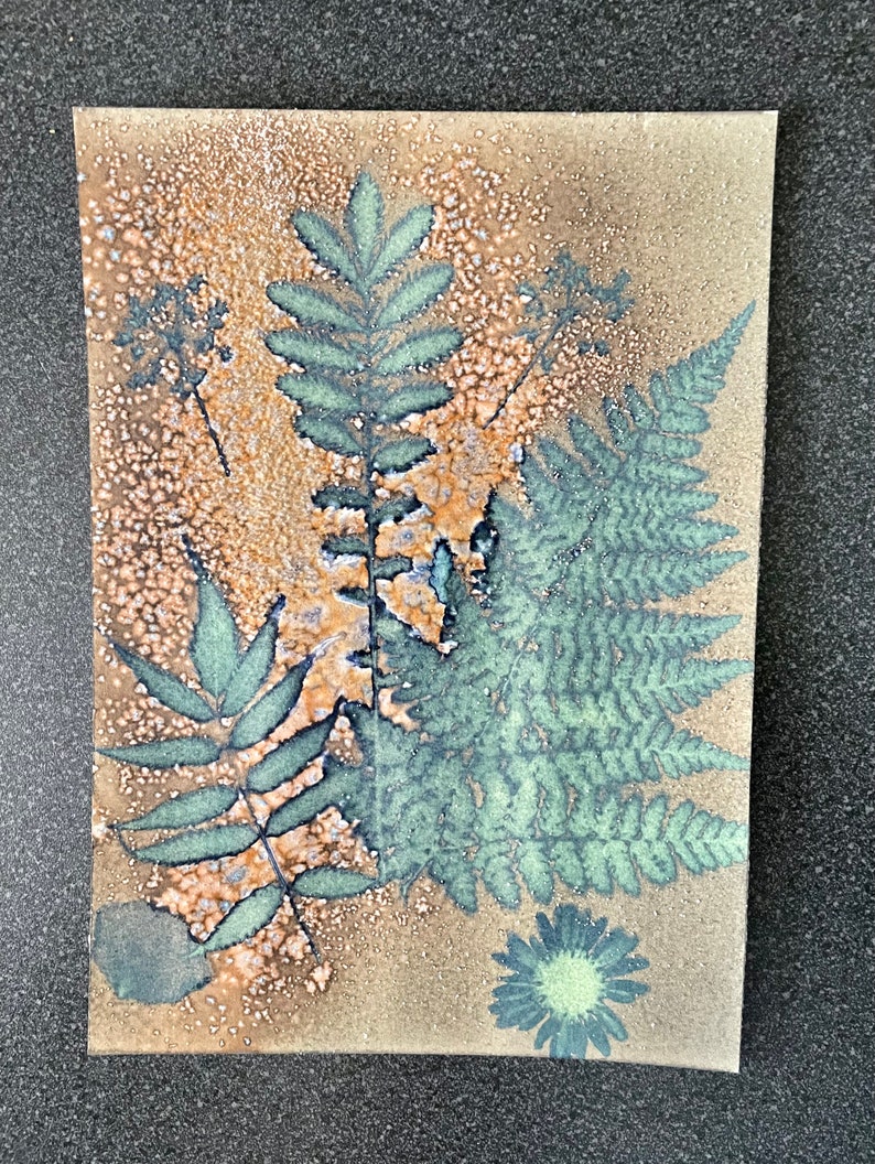 May include: A brown paper background with a green fern leaf, a green flower, and a few other green leaves. The background has a speckled texture.