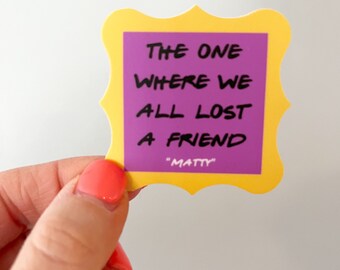 May include: A yellow and purple sticker with the text "THE ONE WHERE WE ALL LOST A FRIEND" and "MATTY" in a yellow frame.