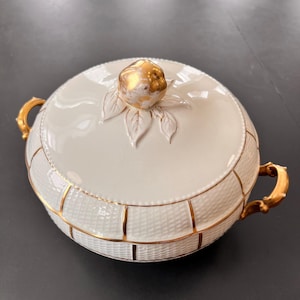 May include: White ceramic serving bowl with a gold rim and a gold leaf design. The lid has a gold apple finial.