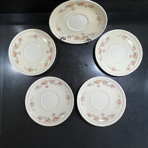 May include: Set of five white ceramic saucers with a floral design in pink, yellow, and green. The saucers have a raised edge and a center depression.