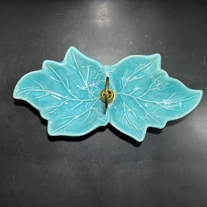 May include: A light blue ceramic serving dish shaped like two leaves with a gold metal handle in the center.
