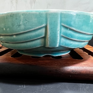 May include: A teal ceramic bowl with a decorative design. The bowl is sitting on a wooden surface.
