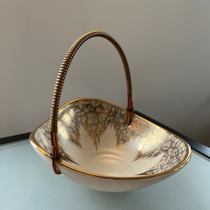 May include: A white ceramic bowl with a gold crackle glaze and a gold rim. The bowl has a brass wire handle.