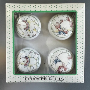 May include: A set of four white ceramic drawer pulls with a green and white polka dot background. Each pull features a different animal design: a bunny, a lamb, a bunny, and a lamb. The box reads "Decorative Drawer Pulls".