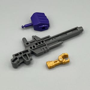 May include: A set of three toy accessories for a robot action figure. The accessories include a purple gun, a gray gun, and a gold hand.