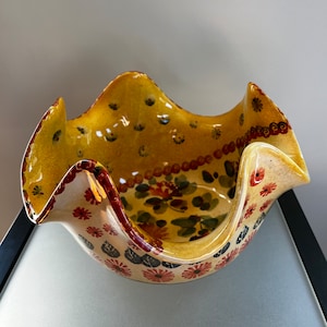 May include: A yellow ceramic bowl with a wavy rim and a floral design in shades of red, green, and black.