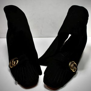 Puede incluir: Un par de mocasines de ante negro con detalles de flecos y logo GG dorado.