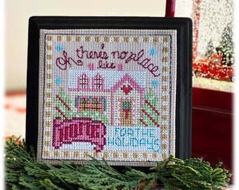 Puede incluir: Bordado de punto de cruz enmarcado en madera negra con fondo beige. El diseño presenta una casa rosa con un camión rojo delante. El texto dice "Oh there's no place like home for the holidays".