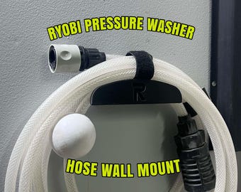 May include: A black Ryobi pressure washer hose wall mount featuring a prominent R logo, holding a coiled translucent white hose with black and light green connectors. The text RYOBI PRESSURE WASHER HOSE WALL MOUNT is displayed in yellow.