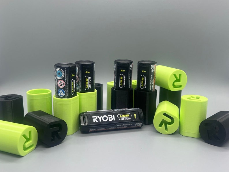 May include: A set of black and green battery storage cases with the text "RYOBI USB LITHIUM" on a black battery charger. The cases are designed to hold batteries for power tools.