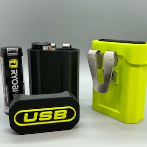 Op de afbeelding: Een zwarte Ryobi lithiumbatterij, een zwarte cilindrische stroomadapter, een zwarte rechthoekige afdekking met de gele tekst USB, en een fel limoengroene stroomadapterbehuizing met een zilveren metalen riemclip aan de zijkant.