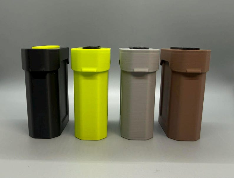 Op de afbeelding: Vier rechthoekige opbergcontainers staan op een rij. De containers zijn zwart, neongeel, lichtgrijs en bruin. Elke eenheid heeft een plat deksel met een klein zwart of geel accentstuk en een verticaal, licht getextureerd lichaam.