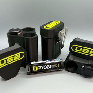 May include: Black USB charging accessories with yellow lettering. Includes a battery, charging ports, and covers. The accessories are designed for use with Ryobi USB lithium batteries. The items are made of black plastic.