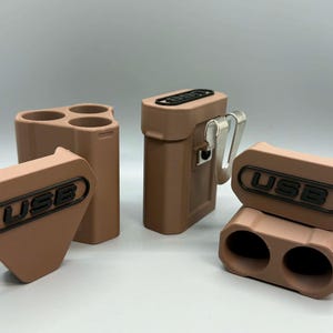 Op de afbeelding: Drie matte, lichtbruine opbergdoosjes voor USB-sticks. E&eacute;n doosje is driehoekig met drie ronde openingen, &eacute;&eacute;n is rechthoekig met een metalen riemclip, en &eacute;&eacute;n is een tweedelige rechthoekige eenheid met twee ronde openingen voor USB-sticks.