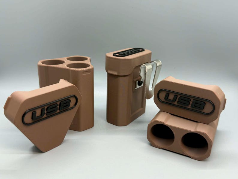 Op de afbeelding: Drie matte, lichtbruine opbergdoosjes voor USB-sticks. E&eacute;n doosje is driehoekig met drie ronde openingen, &eacute;&eacute;n is rechthoekig met een metalen riemclip, en &eacute;&eacute;n is een tweedelige rechthoekige eenheid met twee ronde openingen voor USB-sticks.