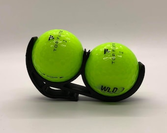 May include: Two bright green golf balls with black lettering that reads "Top Flight 11" and "WLD  World Long Drive" in a black golf ball holder.