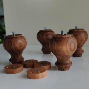 May include: Set of five wooden furniture legs with a turned, bulbous design. The legs are a warm brown color and have a threaded metal insert for attachment. Also included are five round wooden mounting plates.