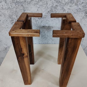 May include: Four wooden table legs, stained a dark brown colour, are assembled in a square shape. The legs are made of thick, sturdy wood and have a rustic, farmhouse style.