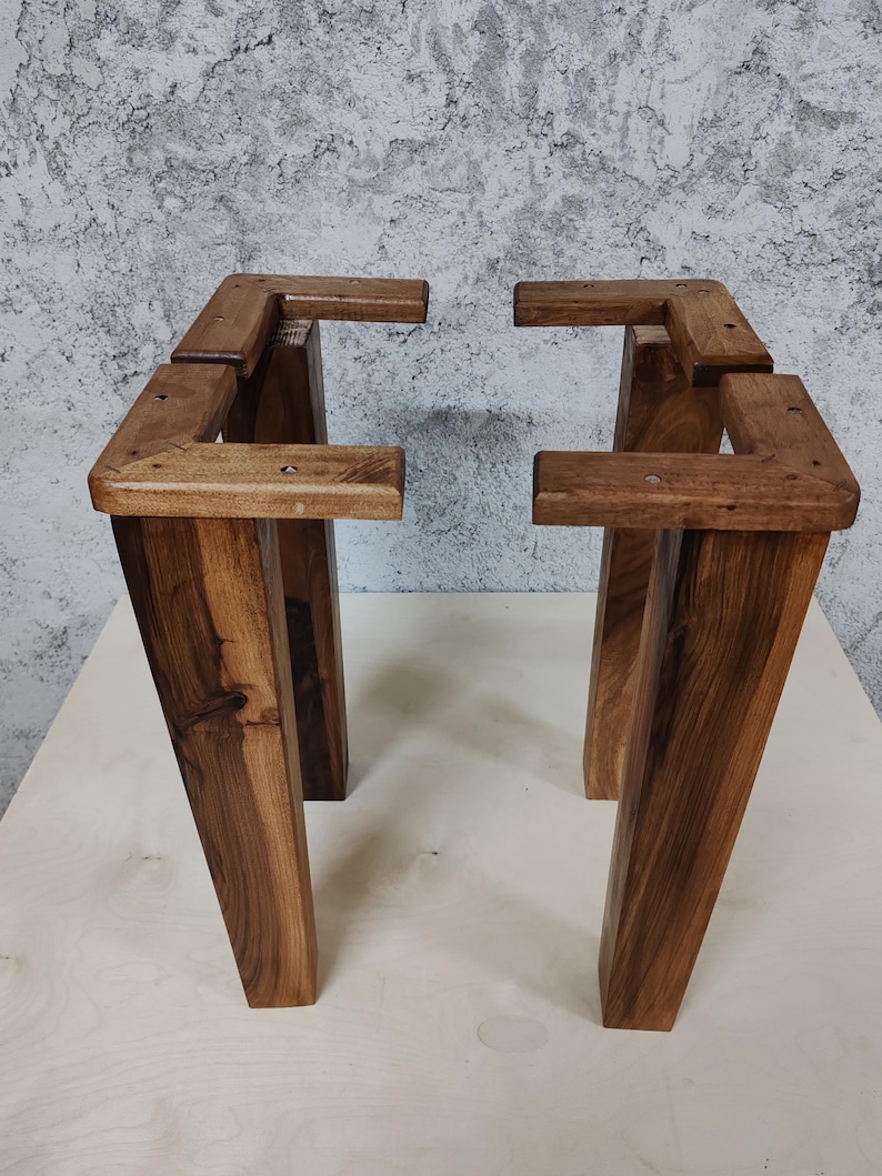 May include: Four wooden table legs, stained a dark brown colour, are assembled in a square shape. The legs are made of thick, sturdy wood and have a rustic, farmhouse style.
